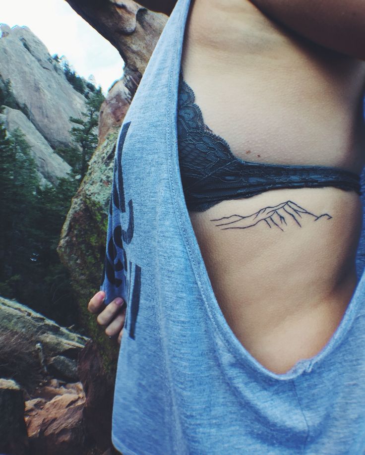 a woman with a mountain tattoo on her stomach is standing in front of some rocks