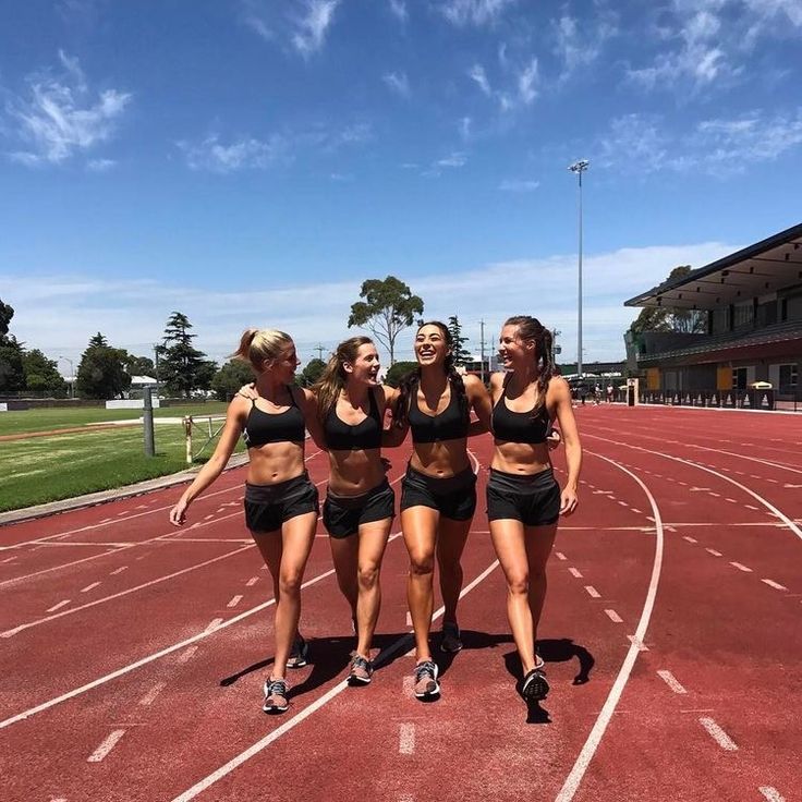 three women in black sports bras are running on a track with their arms around each other