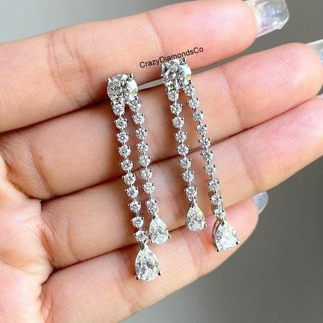 Round & Pear Cut Moissanite Diamond Tennis Drop Earrings, Double Row Stud Dangle Earrings, 14k White Gold Wedding Earrings, Screw Back  ✹✹𝐖𝐞𝐥𝐜𝐨𝐦𝐞 𝐭𝐨 𝐂𝐫𝐚𝐳𝐲𝐃𝐢𝐚𝐦𝐨𝐧𝐝𝐬𝐂𝐨✹✹ Detail about stones Moissanite & Simulated Stone: ----------------------------- Stone Shape: Round & Pear Cut Stone Size: 8X6 mm Weight: 7.26 TCW Color: Colorless Cut: Excellent Clarity: VVS ★ 𝑰𝒕𝒆𝒎 𝑫𝒆𝒕𝒂𝒊𝒍𝒔:- ☛ Metal Purity: Solid Gold (10KT, 14KT, 18KT); Silver(925 Sterling, 935 Argentium), 950 Platinum ☛ Metal Tone: Yellow, White, Rose ☛ Stamp/Hallmark: Yes ★ 𝑪𝒖𝒔𝒕𝒐𝒎𝒊𝒛𝒂𝒕𝒊𝒐𝒏:- ☛ Customized Design Jewelry. ☛ All cuts which you dream to make with moissanite. ☛ Updating every step of your ordered jewelry(Loose Stone, CAD & Making Process) ☛ All listed items in our stores are made to Diamond White Pear-shaped Chandelier Earrings For Anniversary, Pear-shaped Diamond White Chandelier Earrings For Anniversary, Diamond Dangle Bridal Earrings With Prong Setting, Diamond Bridal Earrings With Prong Setting, Diamond White Teardrop Chandelier Earrings For Anniversary, Vvs Clarity Drop Diamond Earrings For Wedding, Anniversary Diamond Drop Crystal Earrings, Diamond White Brilliant Cut Dangle Bridal Earrings, Diamond Drop Crystal Earrings For Anniversary