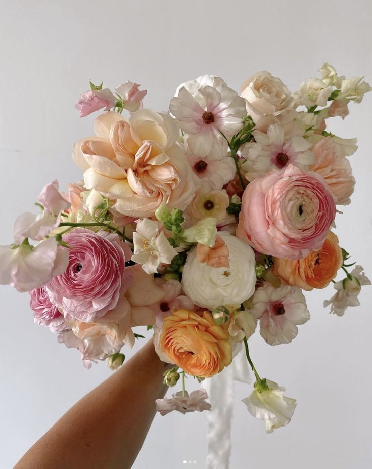 a hand holding a bouquet of flowers on a white tablecloth with pink and orange blooms in it