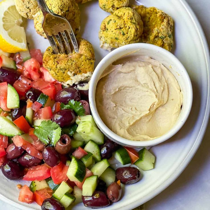 a white plate topped with veggies and meatballs next to a bowl of dip