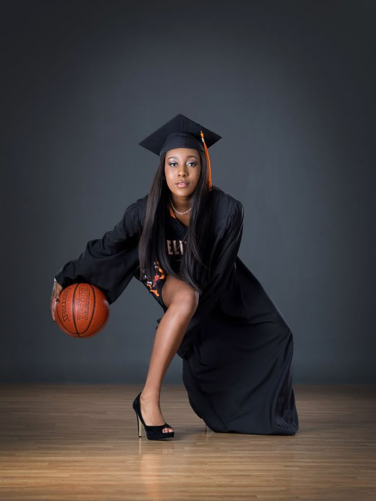 a woman in a graduation gown holding a basketball and posing for a photo on a wooden floor