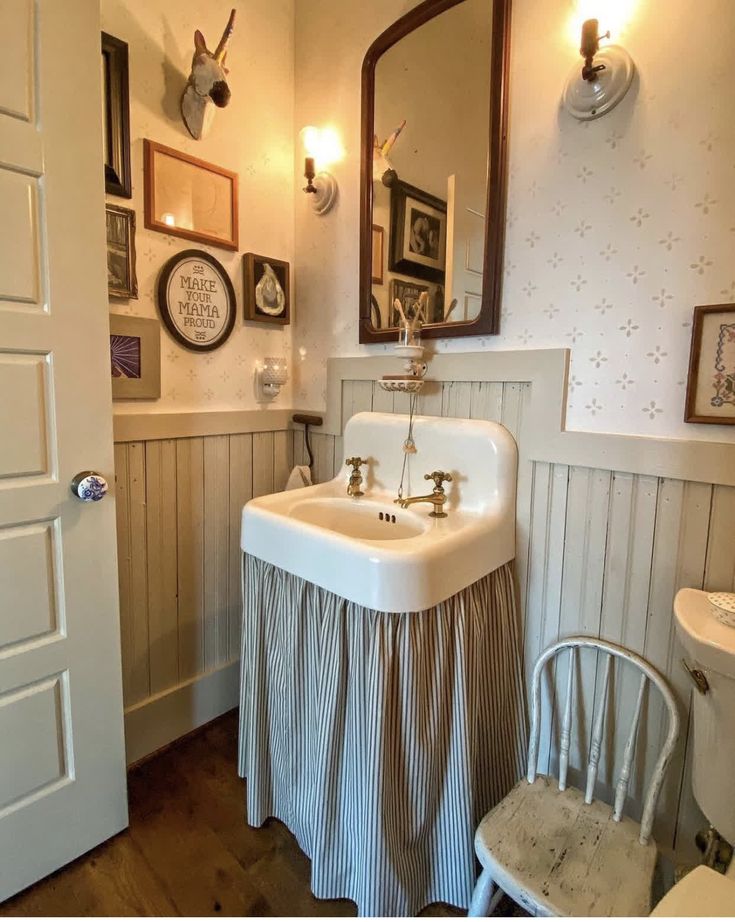 a white sink sitting under a bathroom mirror next to a chair and wall mounted pictures