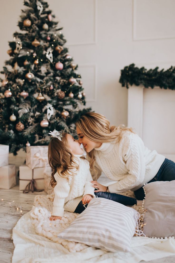 a mother kissing her daughter in front of a christmas tree