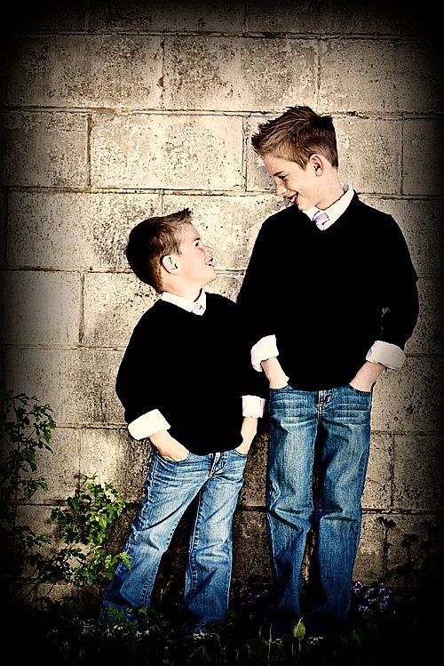 two boys standing next to each other in front of a brick wall