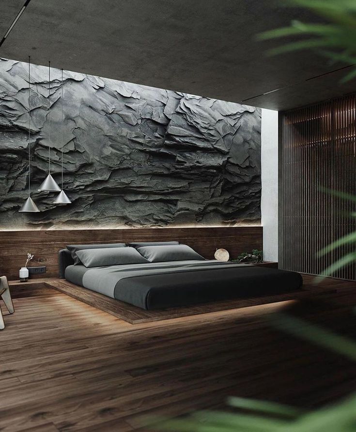 a bedroom with wood flooring and large stone wall behind the bed in front of it