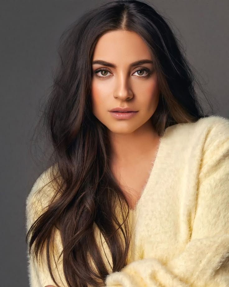 a woman with long dark hair wearing a white sweater and posing for a studio photo