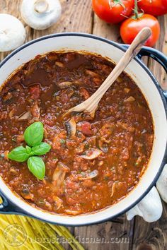 a large pot filled with chili and mushrooms next to garlic, tomatoes, peppers, and other vegetables