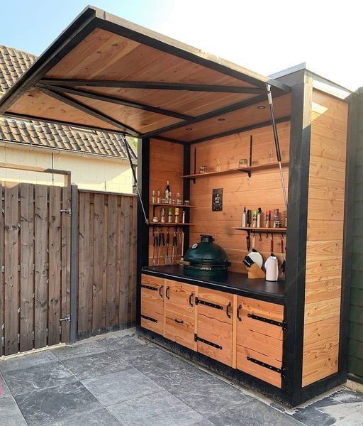 an outdoor kitchen is built into the side of a house with wooden cabinets and shelves