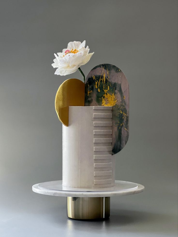 a white flower sitting on top of a table next to a vase with a gold disc