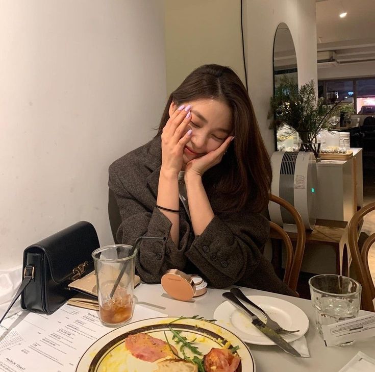 a woman sitting at a table in front of a plate of food with her hands on her face