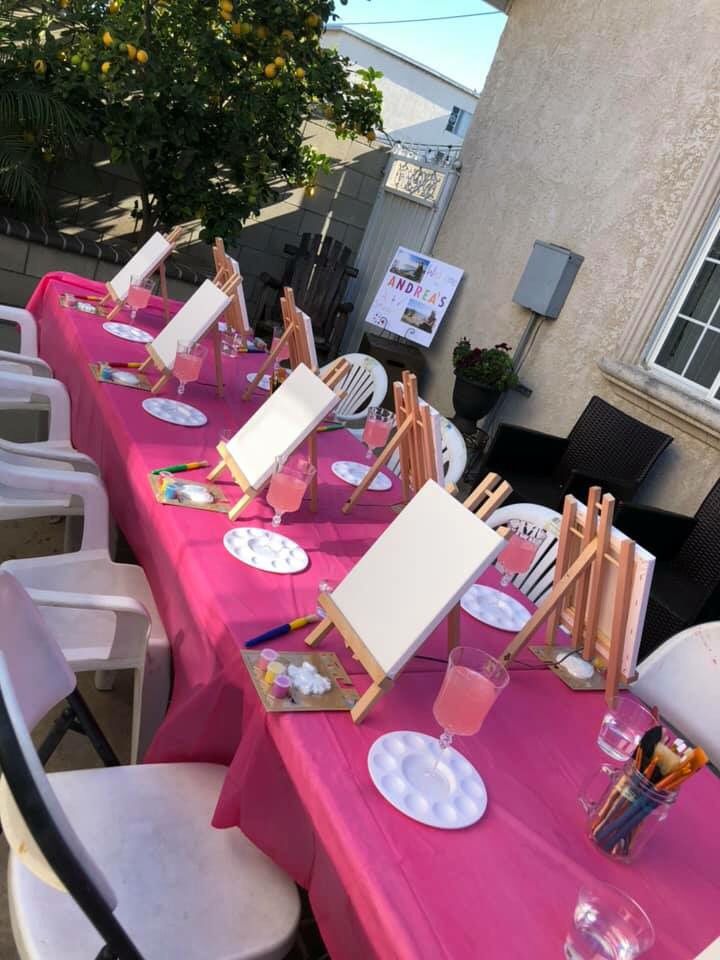 there are many paintings on the tables at this outdoor event that is decorated with pink tablecloths and white chairs