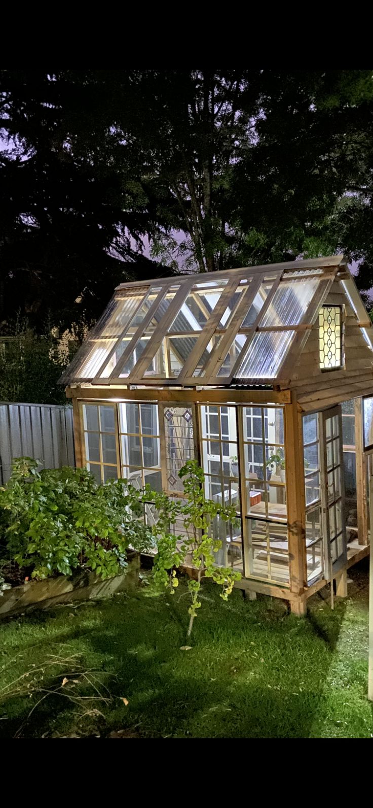 a small wooden greenhouse in the middle of a yard at night with lights shining on it