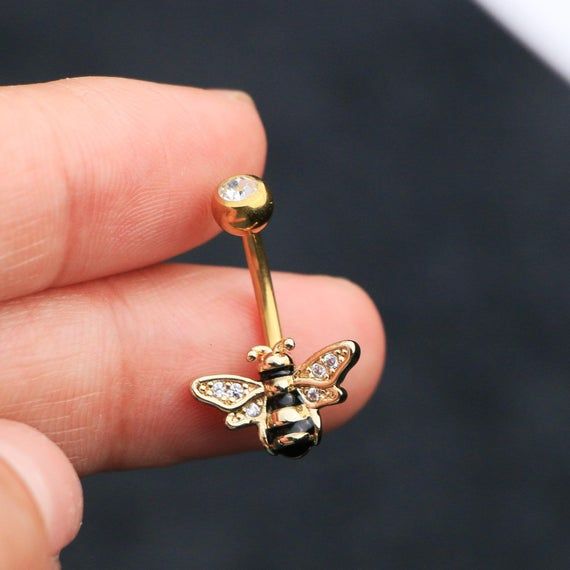 a person is holding a gold nose ring with a diamond bee on it's side