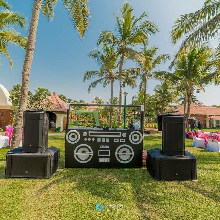 an outdoor party setup with speakers and dj's in the grass near palm trees