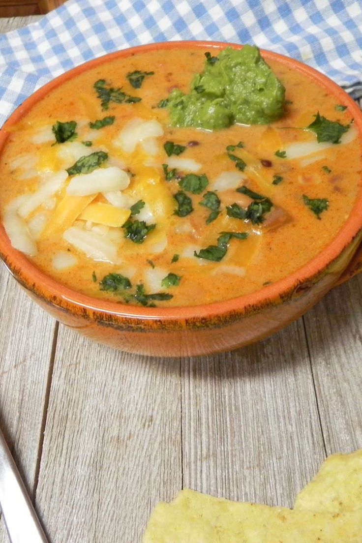 a bowl of soup with tortilla chips and guacamole on the side