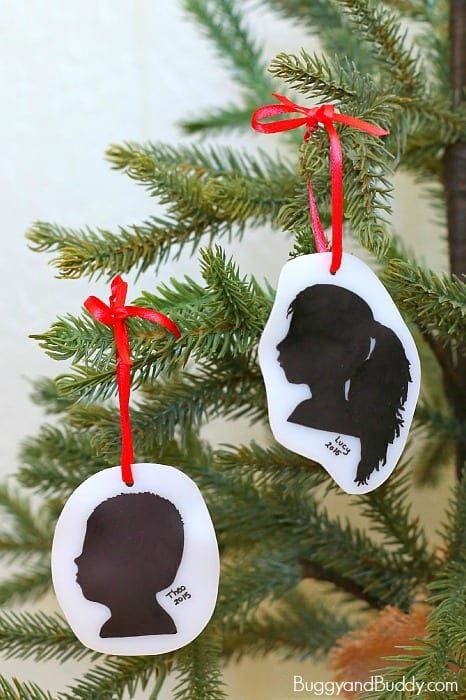 two ornaments hanging from a christmas tree decorated with silhouettes of children's heads