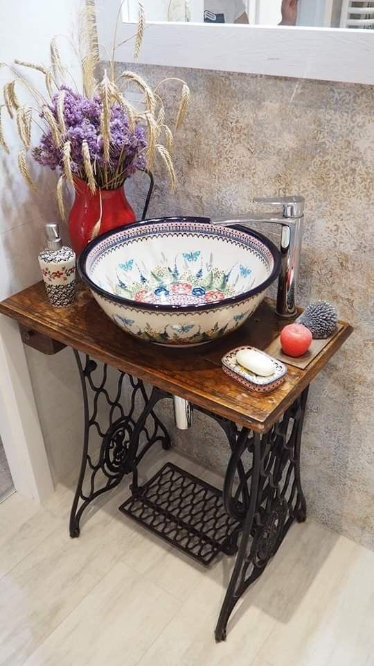 an old sewing table with a bowl on it and some flowers in the vase next to it