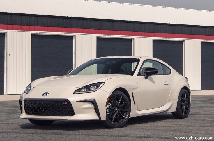 a white toyota sports car parked in front of a garage door with two doors open