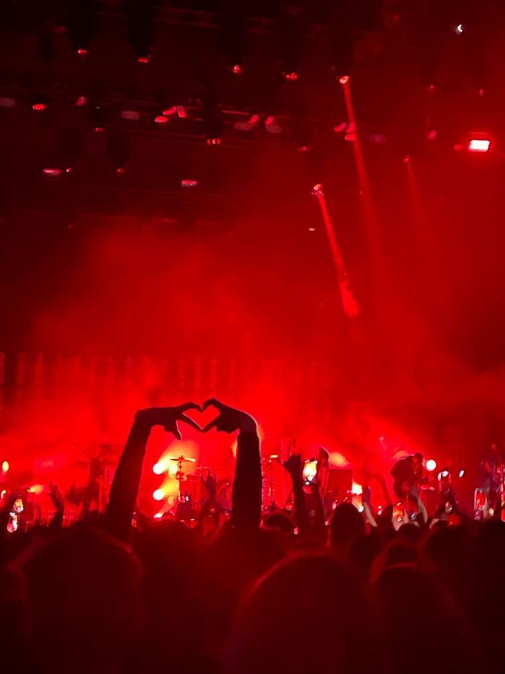 a crowd at a concert with their hands up in the air and red lights behind them