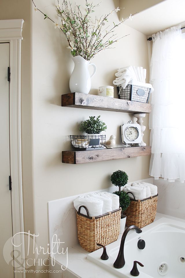 bathroom shelves with baskets and towels on them in front of a bathtub filled with flowers