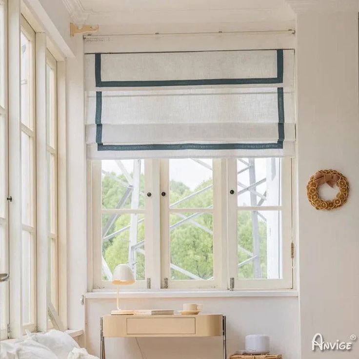 a bed sitting under a window next to a wooden table and white walls in a bedroom