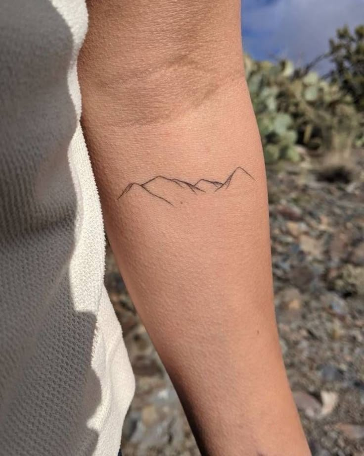 a woman's arm with a small mountain tattoo on the left side of her arm