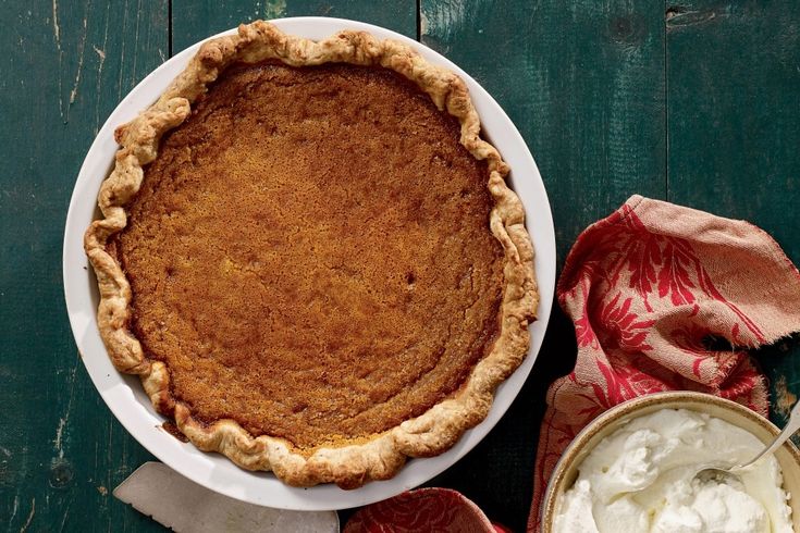 a pie sitting on top of a white plate next to a bowl of whipped cream