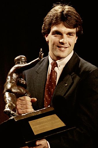 a man in a suit and tie holding up a trophy while standing next to a statue