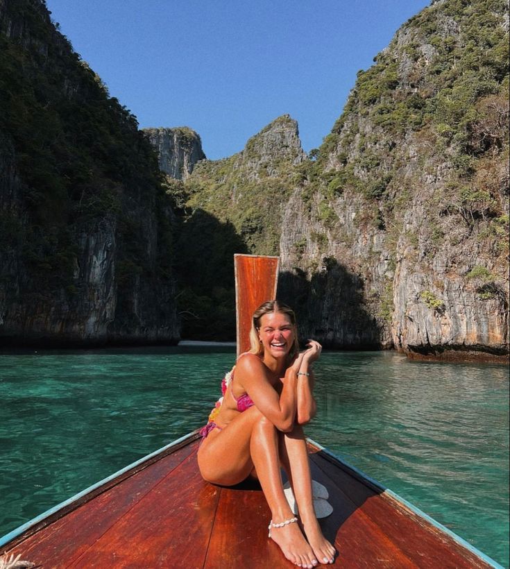 a woman sitting on the bow of a boat in front of some mountains and water