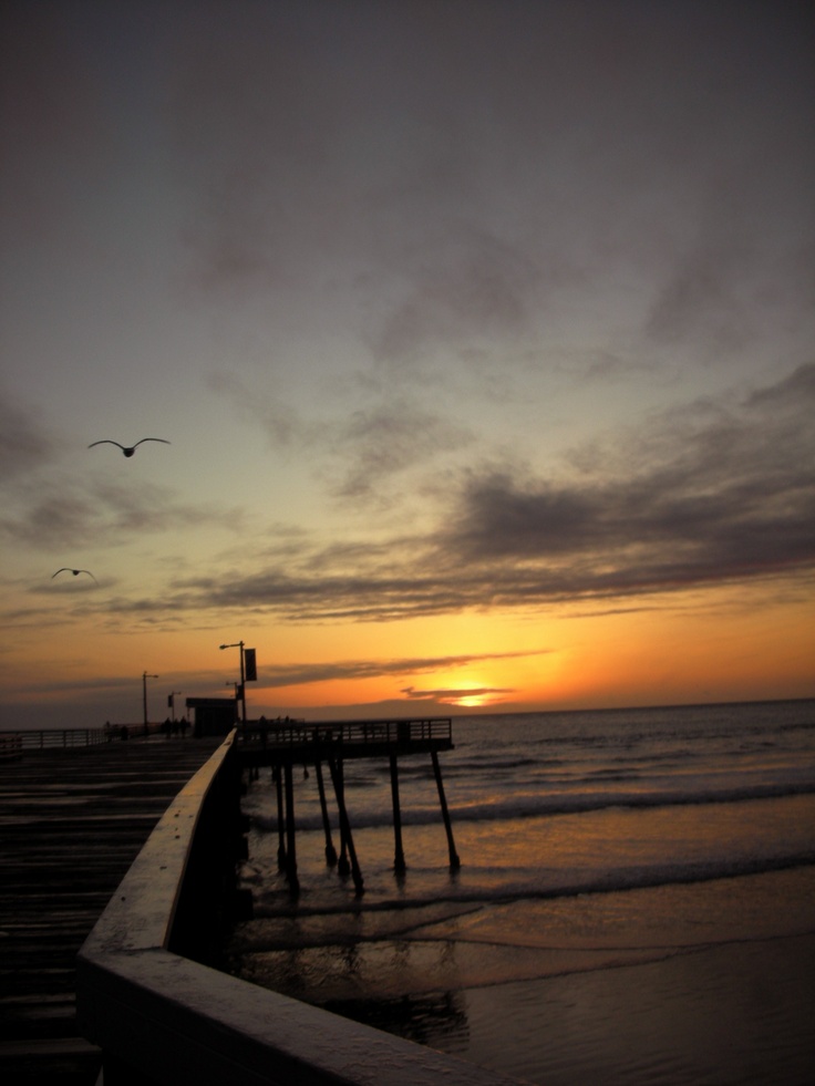 the sun is setting at the end of the pier