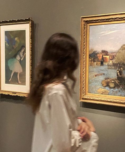 a woman standing in front of two paintings on the wall and looking at it with her back to the camera