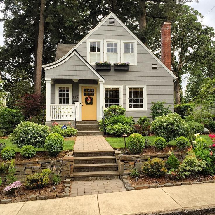 a gray house with yellow door and steps leading up to the front door, surrounded by trees