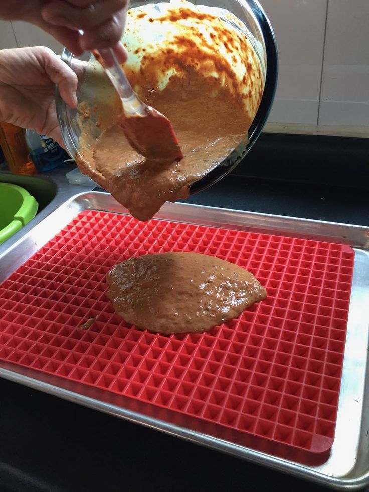 a person pouring peanut butter onto a cookie sheet