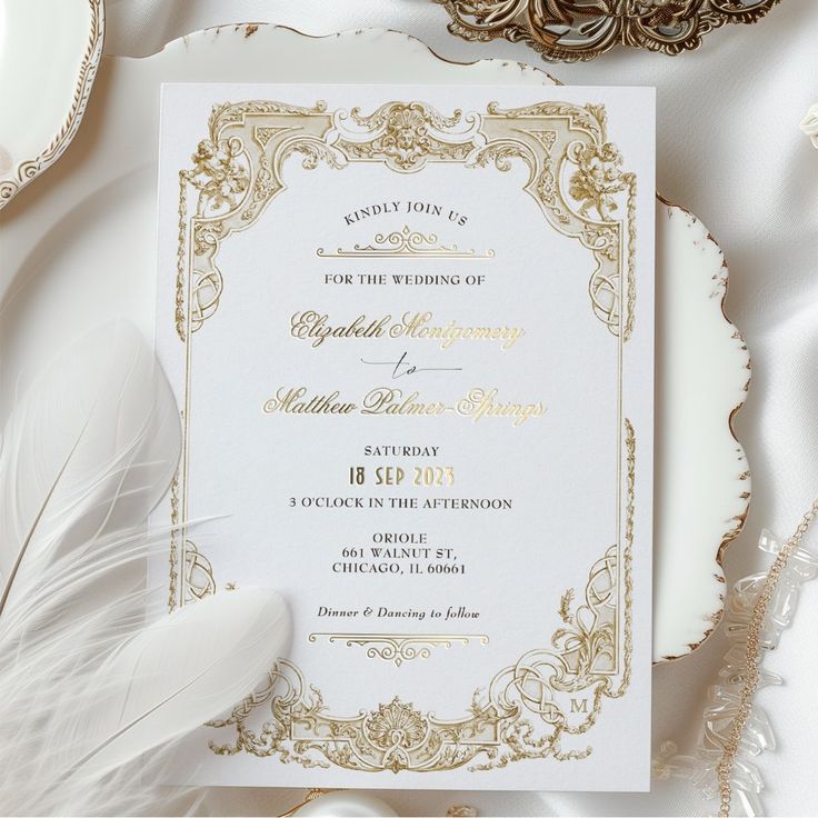 a white and gold wedding card on top of a plate next to some silverware