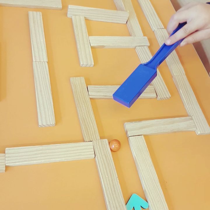 a person using a blue toothbrush to cut out letters on a yellow surface with pegs