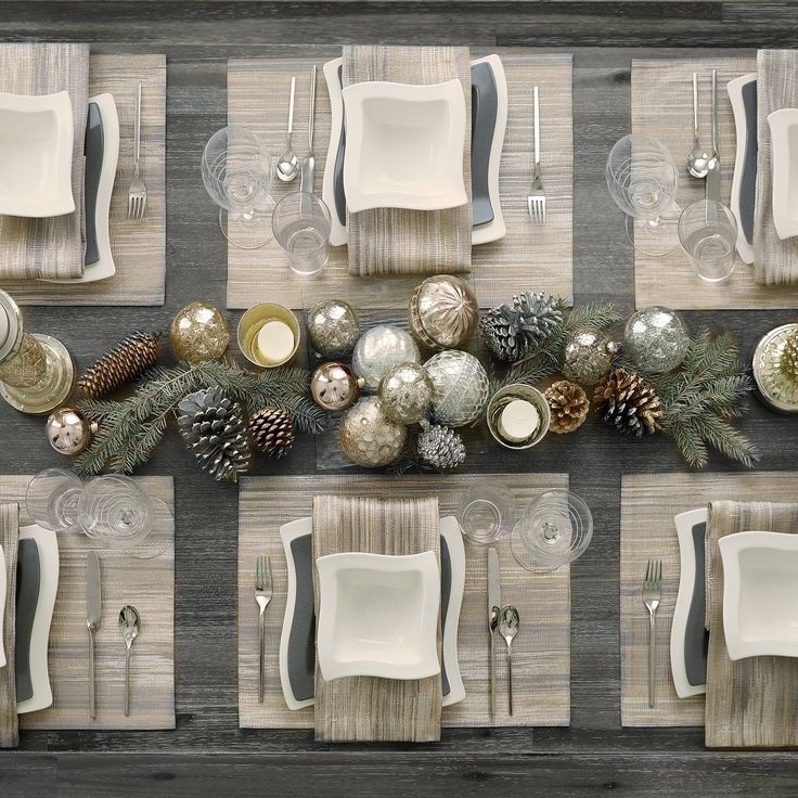 the table is set for christmas dinner with silver and white dishes, pine cones, napkins