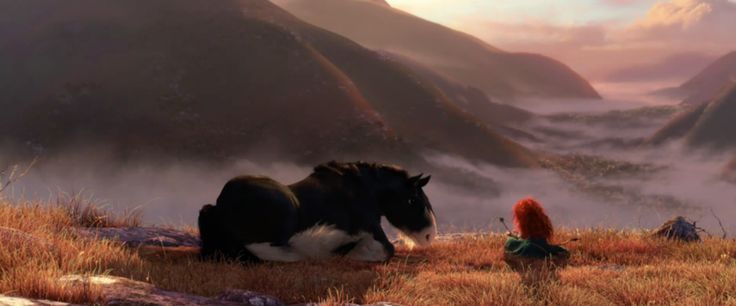 there is a horse that is sitting in the grass with mountains and clouds behind it