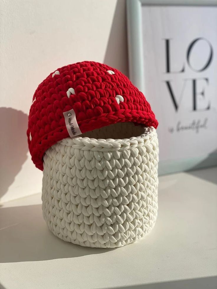 a knitted red hat sitting on top of a white basket next to a love sign