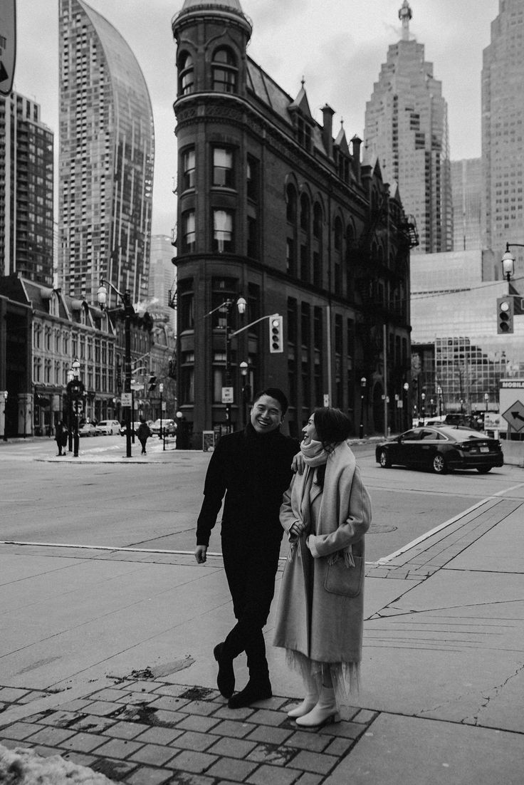 a man and woman are walking down the sidewalk in front of some tall buildings on a cloudy day