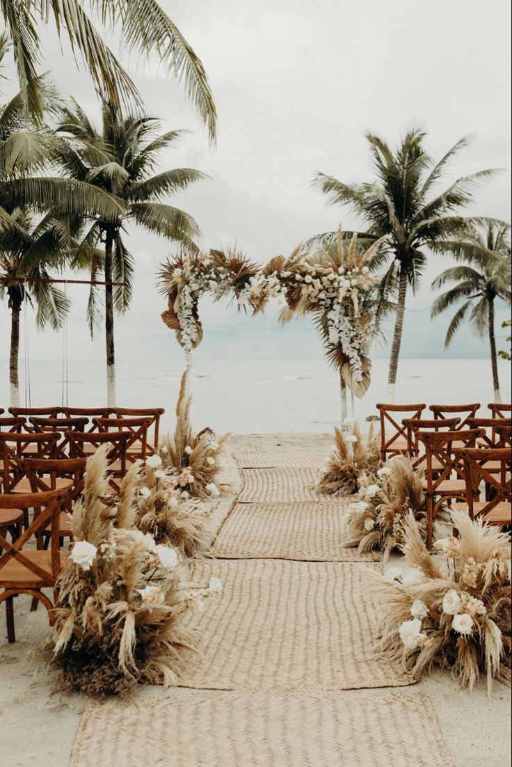 an outdoor ceremony set up on the beach with chairs and palm trees in the background