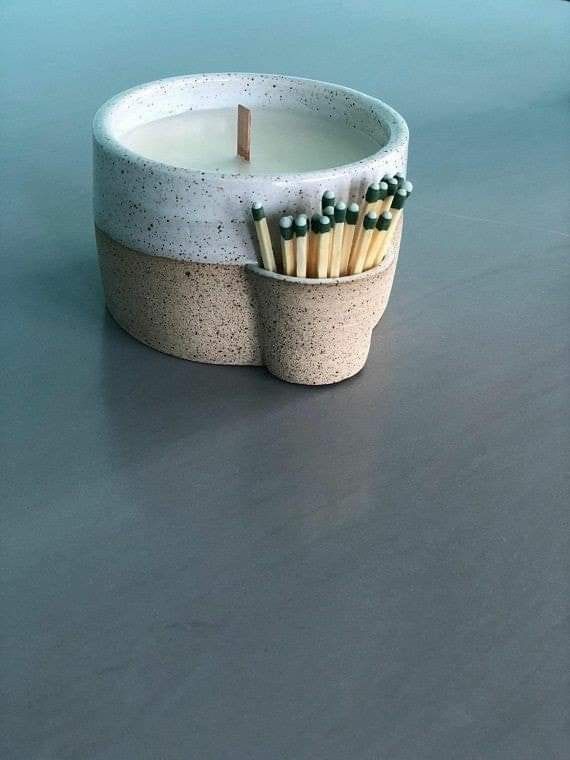 a candle holder with matches in it sitting on a gray table next to other candles