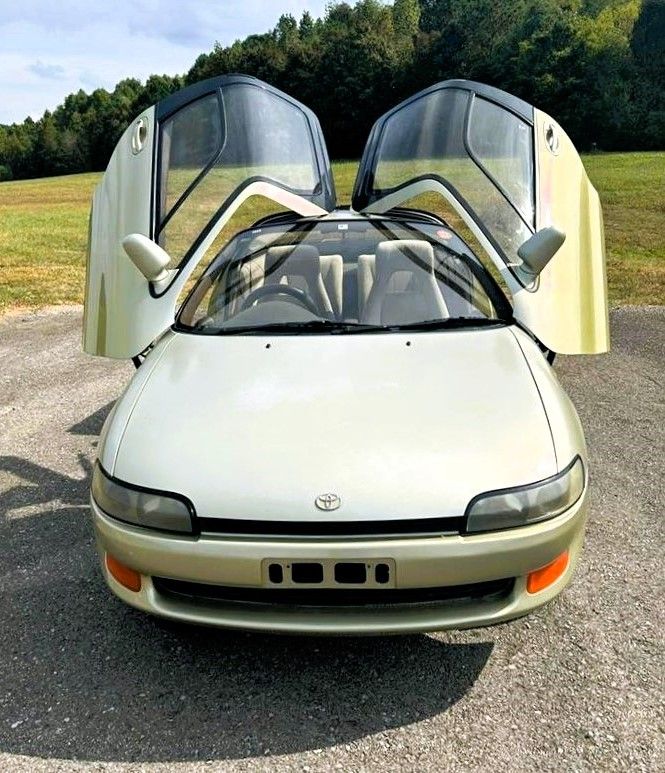 a car with its doors open sitting in the middle of a parking lot next to a field