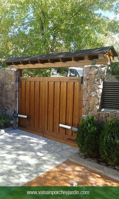 a wooden gate in front of a stone wall and green plants on the side walk