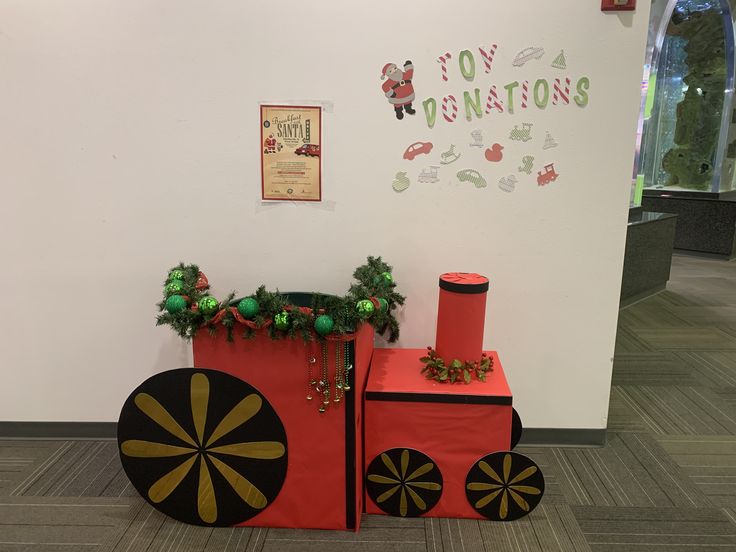 a red train sitting on top of a floor next to a white wall with christmas decorations