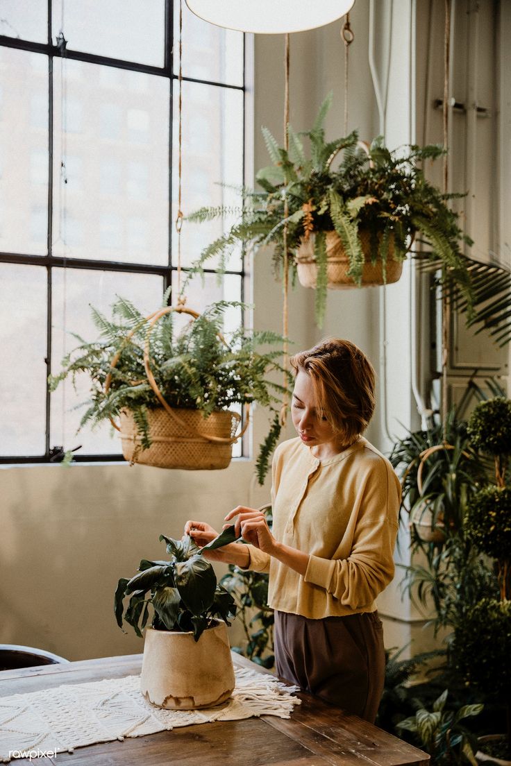 a woman standing in front of a potted plant on top of a wooden table