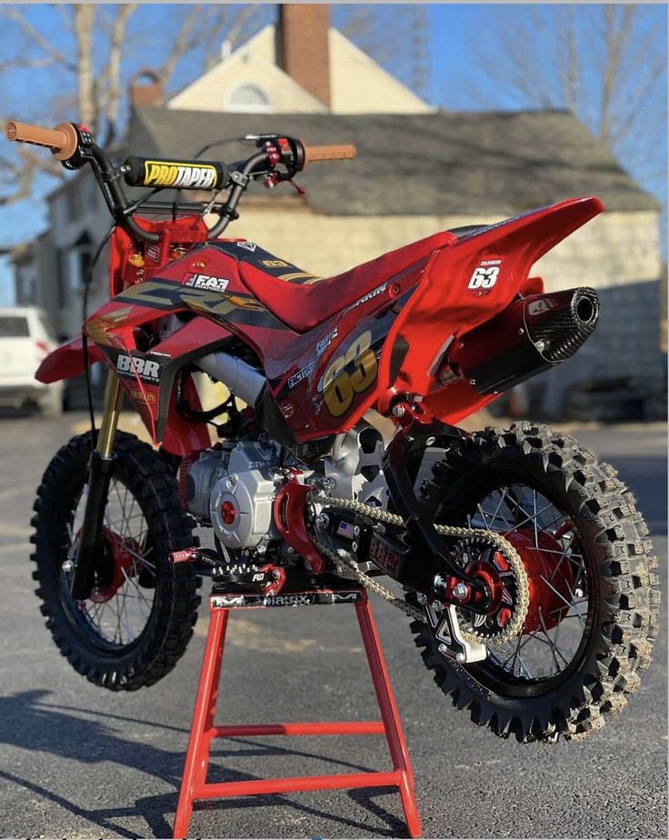 a red dirt bike parked on top of a metal stand in a parking lot next to a building