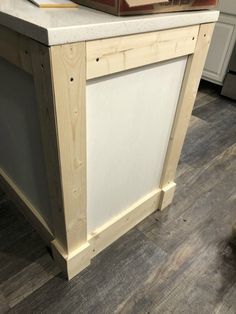 a kitchen island made out of plywood planks and white painted cabinetry with a book on top