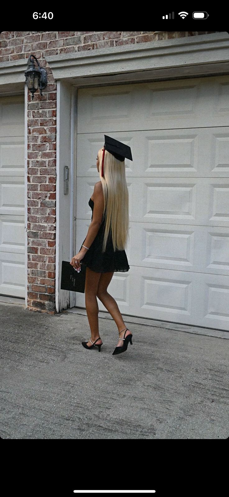 a woman with long blonde hair walking in front of a garage door wearing a graduation cap and gown