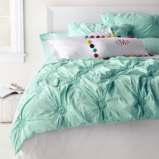 a bed with green comforter and pillows on top of it in a white room